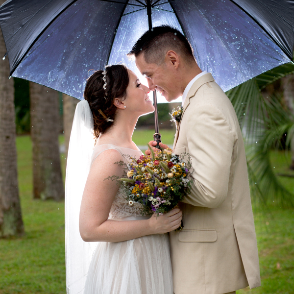 A couple embraces under an umbrella on their rainy wedding day at Atalaya Castle
