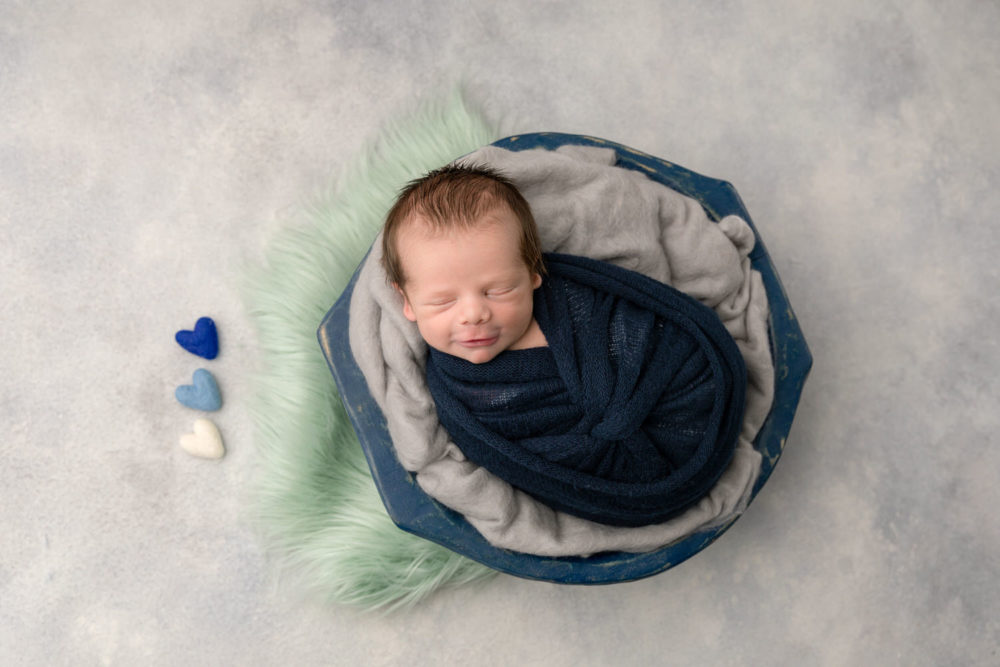 Smiling newborn boy in a navy blue, grey & teal set